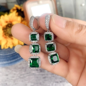 Detail of drop earrings featuring emerald-cut green gems and sparkling zircon halo