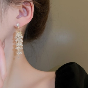 Vue latérale de longues boucles d'oreilles à pompons dorés et perles sur un mannequin