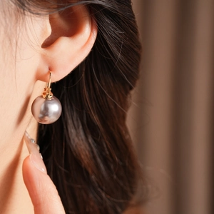 Close-up of a model wearing a dusty pink pearl drop earring with gold metal hardware