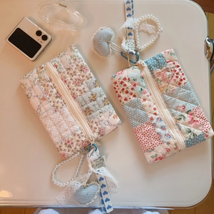 Blue floral quilted makeup bag with lace edges and a pearl charm in a flat lay view