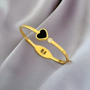 Detailed close-up of a gold heart bangle with black inlay and crystal on grey satin fabric