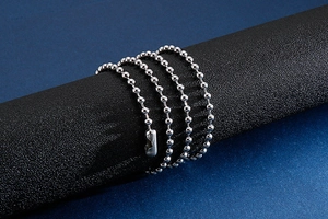 Détail d'un collier chaîne à billes en acier argenté enroulé sur un cylindre noir