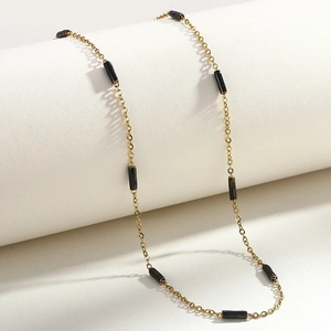 Collier minimaliste en acier inoxydable doré avec petites perles noires sur support blanc