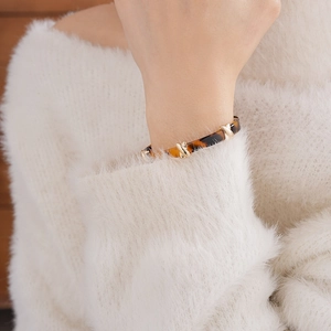 Close-up of leopard resin bangle with gold buckle worn on a white knit sleeve wrist