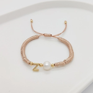 Detail of woven champagne cord bracelet featuring a white pearl and gold letter Z