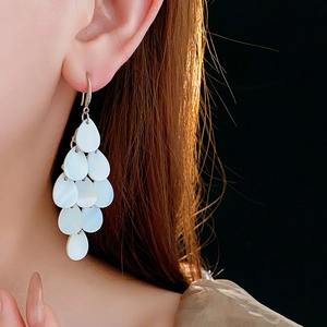 Detailed view of white teardrop shell tassel earrings worn by a model on black background