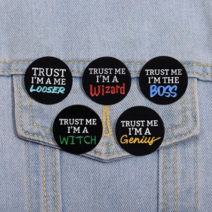Detailed view of five black enamel pins with TRUST ME quotes on a denim jacket