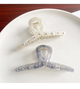 Detail of white and grey-blue acetate hair claws with rhinestones on ceramic plate