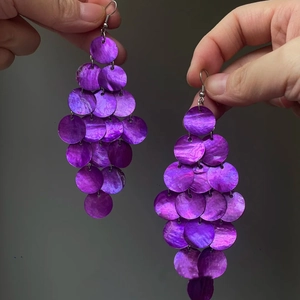 Makro-Detail violetter Muschelscheiben an silbernen Boho-Ohrhaken in der Hand