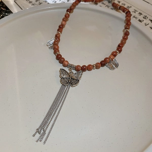Detail showing vintage brown beads necklace with silver butterfly pendant and metal tassels