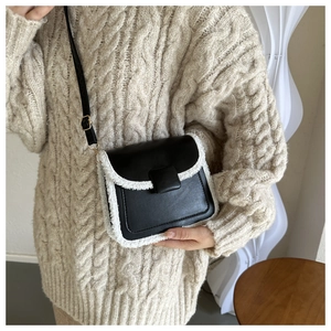 Close-up of retro black square bag with white shearling trim worn with a beige sweater