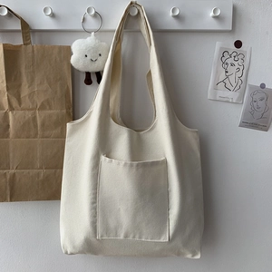 Detail of minimalist beige canvas tote bag with front pocket shown on white wall