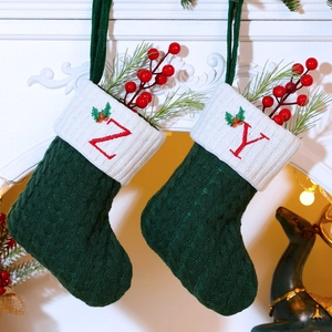 Detail of green knitted Christmas stocking with embroidered red letters and holly decor