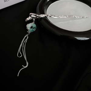 Detail of silver hair stick with green translucent pendant and metal tassels on black base