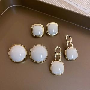 Flat lay of cream white resin earrings with gold metal frames on a brown tray