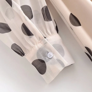 Détail de la manche bouffante beige à pois noirs avec un bouton blanc au poignet