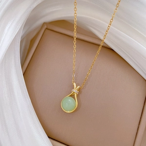 Detailed close-up of a gold waterdrop necklace with green stone on white silk