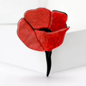 Detail of red enamel rose brooch with gold glitter and black stem on white background
