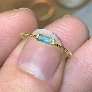 Detail of gold hammer-textured ring featuring a rectangular blue gemstone held by hand