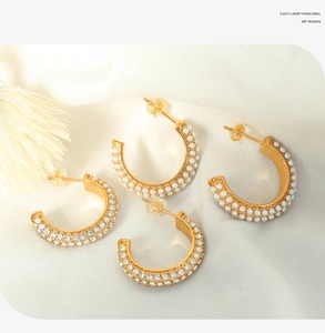 Macro view of C-shaped gold earrings with double-row pearls and crystals on silk fabric