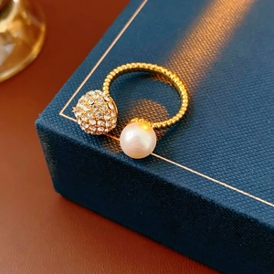 Macro detail of gold open ring featuring a white pearl and crystal-encrusted sphere