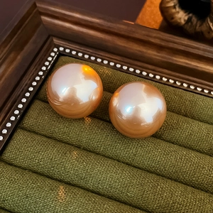 Macro shot of large round champagne gold pearl earrings on dark green velvet background