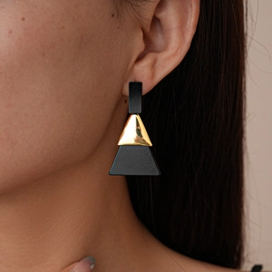 Gros plan sur des boucles d'oreilles géométriques en acrylique noir mat et or sur un modèle