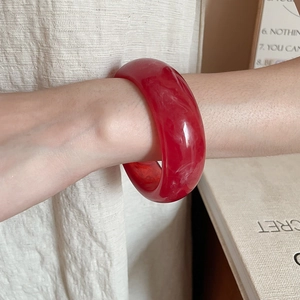 Detail of dark red resin bangle with marble texture on wrist against cozy background