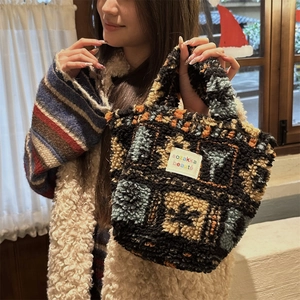 Detail of plush plaid tote bag with sozakka beaute label held in a cozy indoor setting