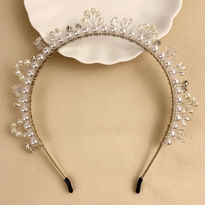 Detail shot of silver headband with pearls and crystals on a textured beige surface