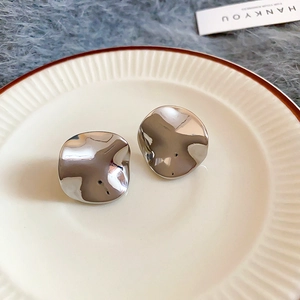 Detailed view of irregular silver liquid metal earrings on an elegant ceramic plate