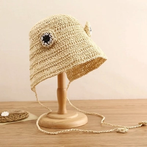 Detailed view of handmade straw frog hat with cute eye decorations and long chin straps