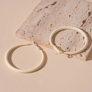 Detailed view of minimalist cream-colored hoop earrings resting on a natural travertine stone