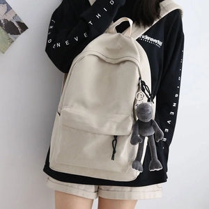 Clean indoor shot of minimalist beige canvas backpack with gray plush toy charm on model