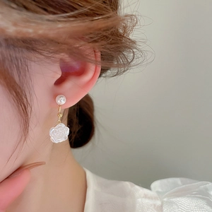 Close-up of white rose petal earrings with a pearl stud on a model's ear