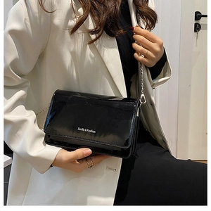 Detail of glossy black patent leather bag with silver chain strap on white blazer