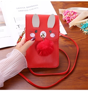 Detail of red rabbit phone bag with plush ball charm and gold chain strap held by hand