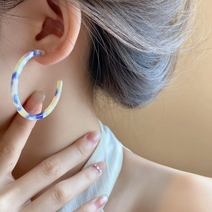 Detail of large C-shaped resin hoop earrings with blue and yellow marble texture