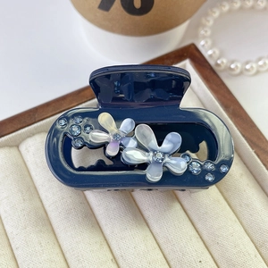 Detail shot of navy blue acetate flower hair claw with rhinestones in a jewelry box