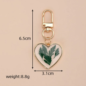Detail showing dimensions of heart-shaped keychain with dried green leaves in gold frame