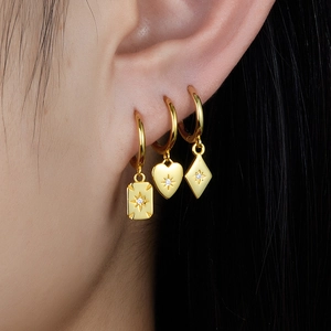 Macro view of three gold S925 silver hoop earrings with heart and square charms on ear