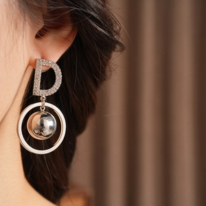 Close-up of silver-toned letter D stud earring with zircon inlay and hanging metal sphere