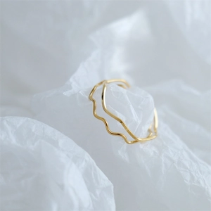 Close-up of a slim wavy gold-plated ring on a textured white fabric background