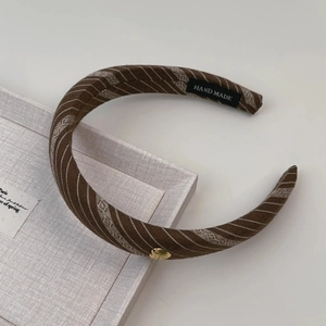 Détail d'un serre-tête en tissu à rayures marron avec un petit accent de cœur doré