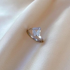 Macro shot of silver butterfly ring with frosted wings on luxury silk fabric