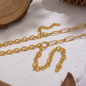 Détail d'un collier chaîne asymétrique doré avec maillons variés sur un fond rustique