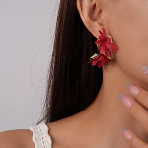 Macro view of red chiffon fabric flower earrings with gold metal accents on a model