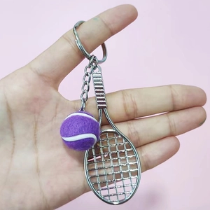 Close-up of a purple tennis ball and silver racket keychain held against pink background