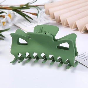 Detail of green matte plastic geometric hair claw clip on white surface with plants