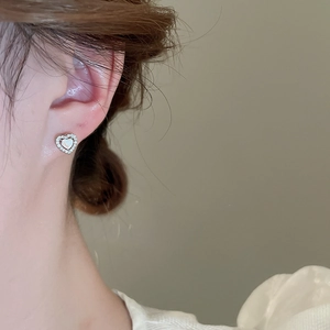 Close-up of heart stud earring with opal inlay and sparkling stones on ear lobe